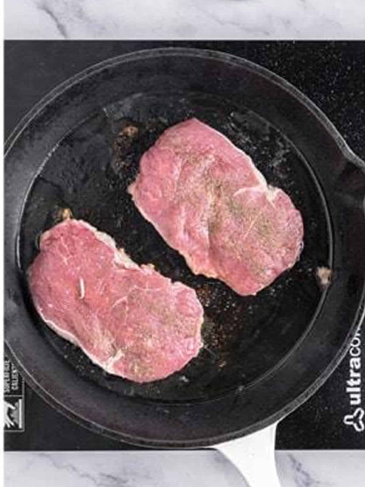 Ribeye steaks searing in a hot skillet for steak pizzaiola.