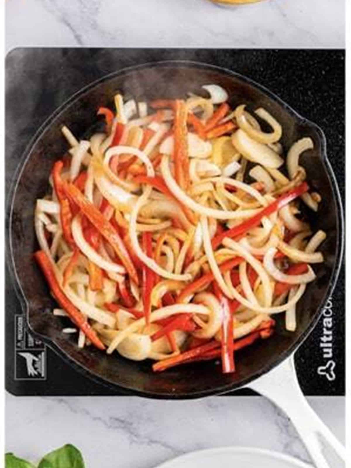 Sliced onion and red bell pepper sauteing in a skillet.