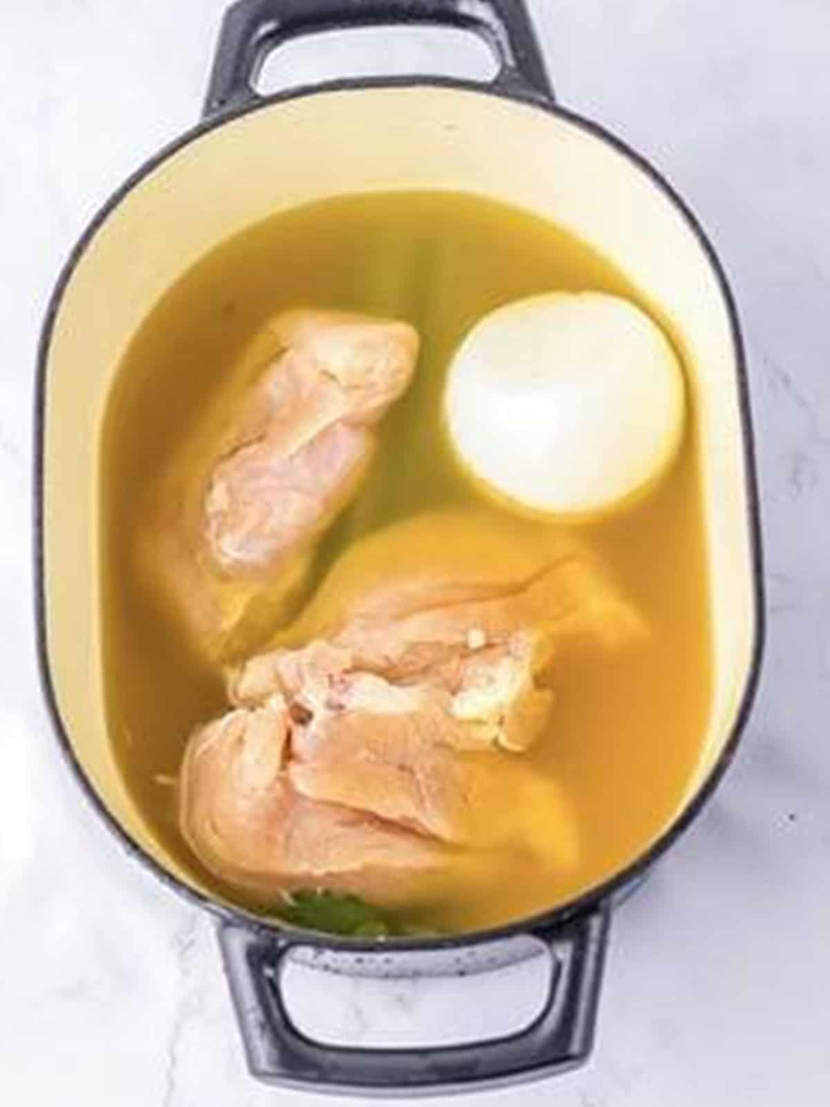Chicken breasts simmering in chicken stock with onion and celery in a pot.