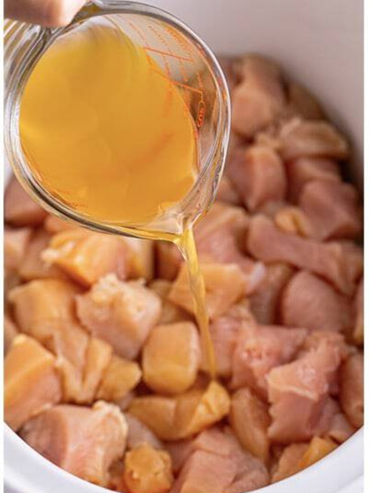 Pouring chicken stock over chicken bites in a slow cooker.