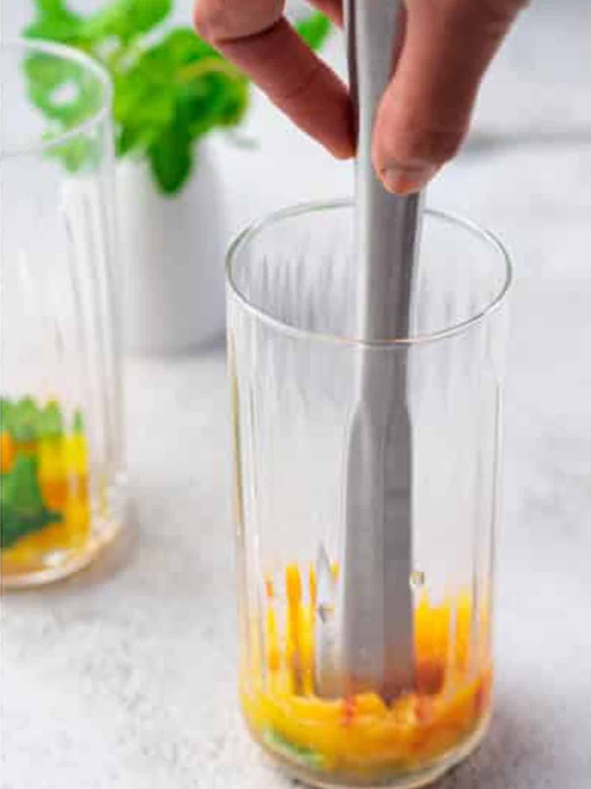 Muddling fresh peach and mint in a tall glass for peach tea.
