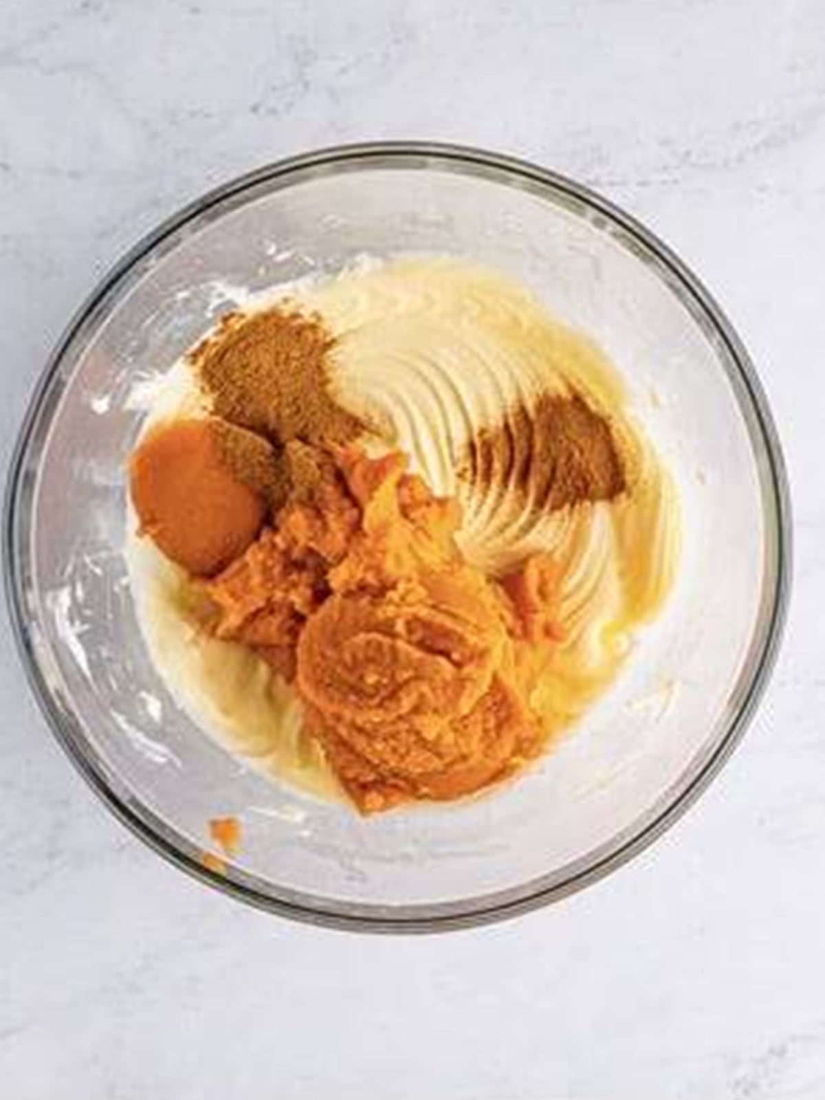 Pumpkin puree and spices added to whipped cream cheese in a bowl.