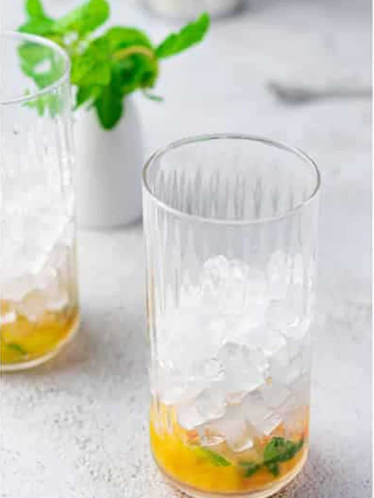Filling a glass with ice over muddled peach and mint.