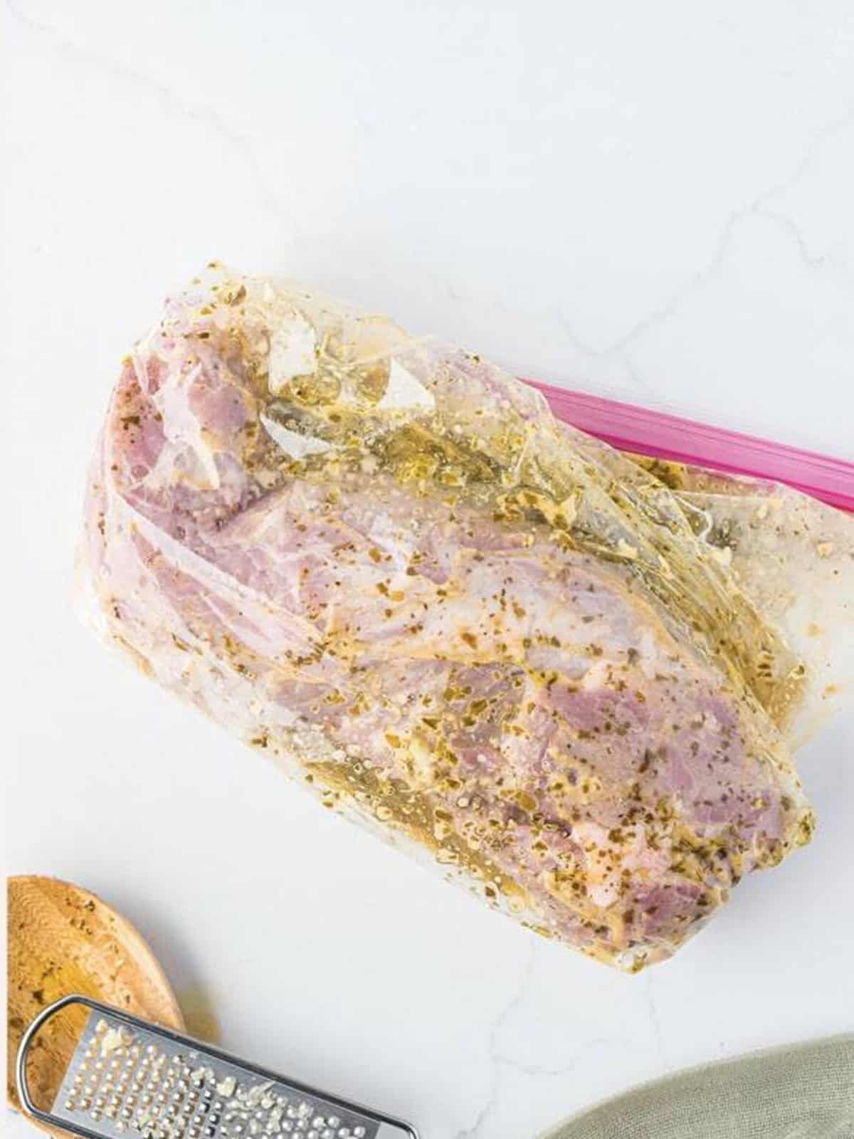 Pork tenderloin marinating in pesto marinade in a zip-top bag.