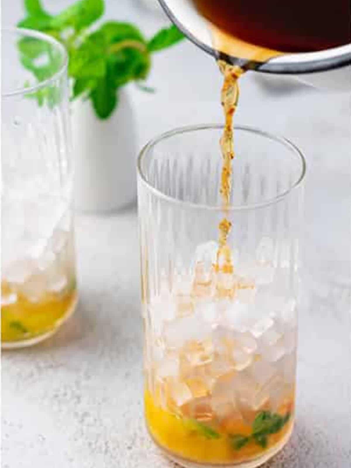 Pouring cooled black tea over ice in a glass for peach tea.