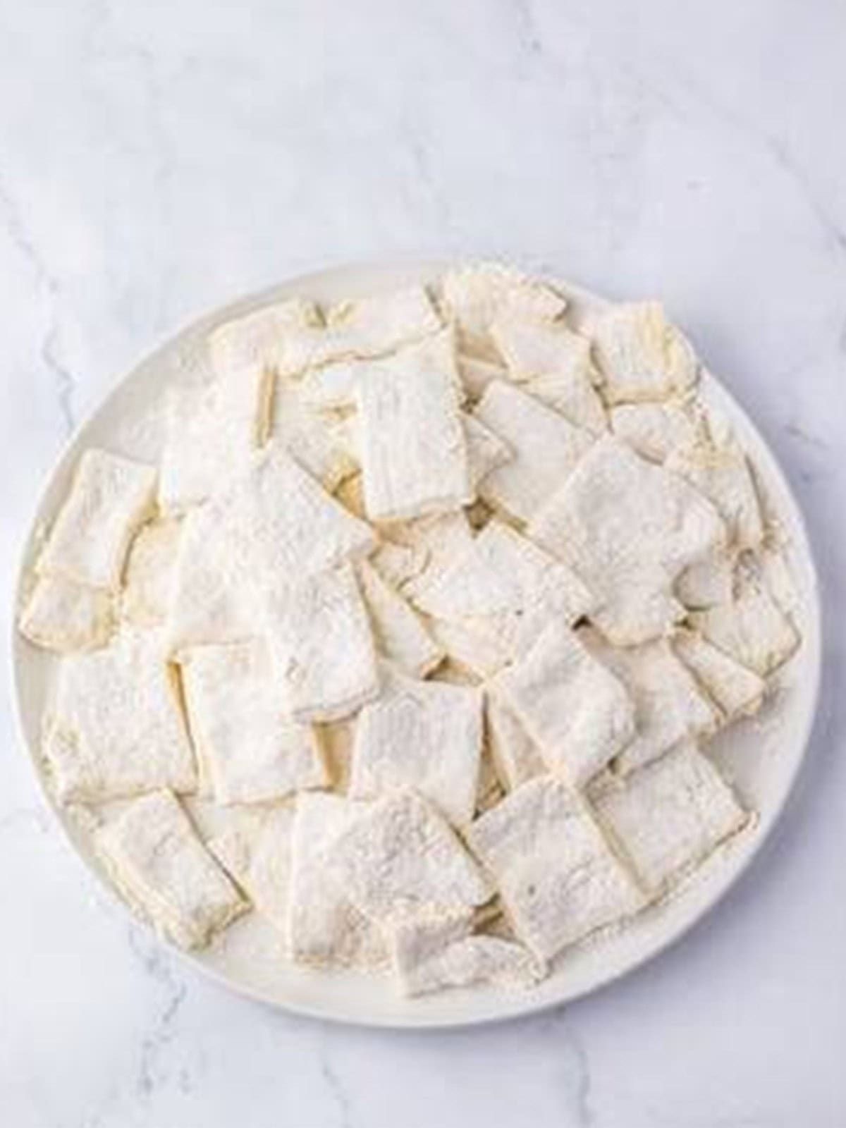 Dumpling dough sliced into one inch squares on a plate.