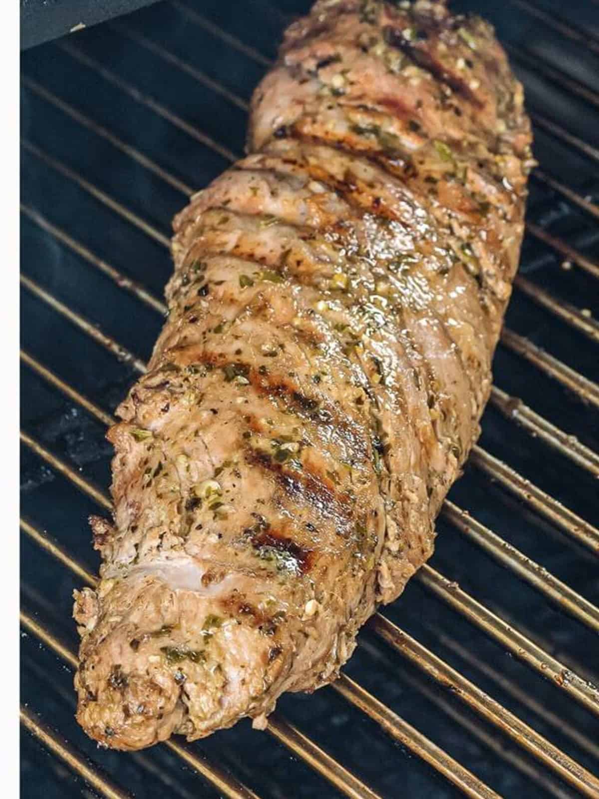 Pork tenderloin grilling on the grill grates until golden.