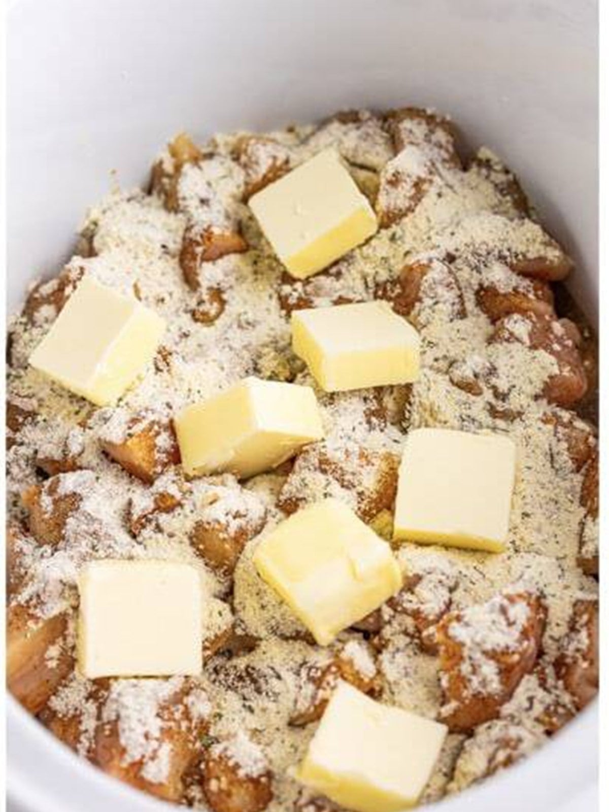 Pats of butter added to seasoned chicken bites in a slow cooker.