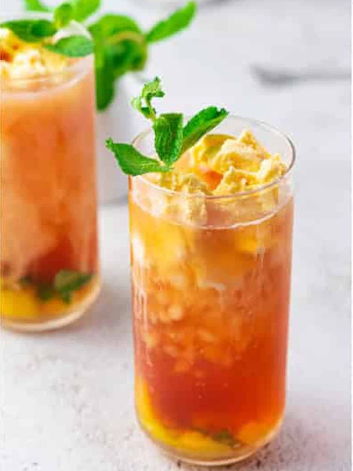 Peach tea topped with a scoop of vanilla ice cream and garnished with peach and mint.