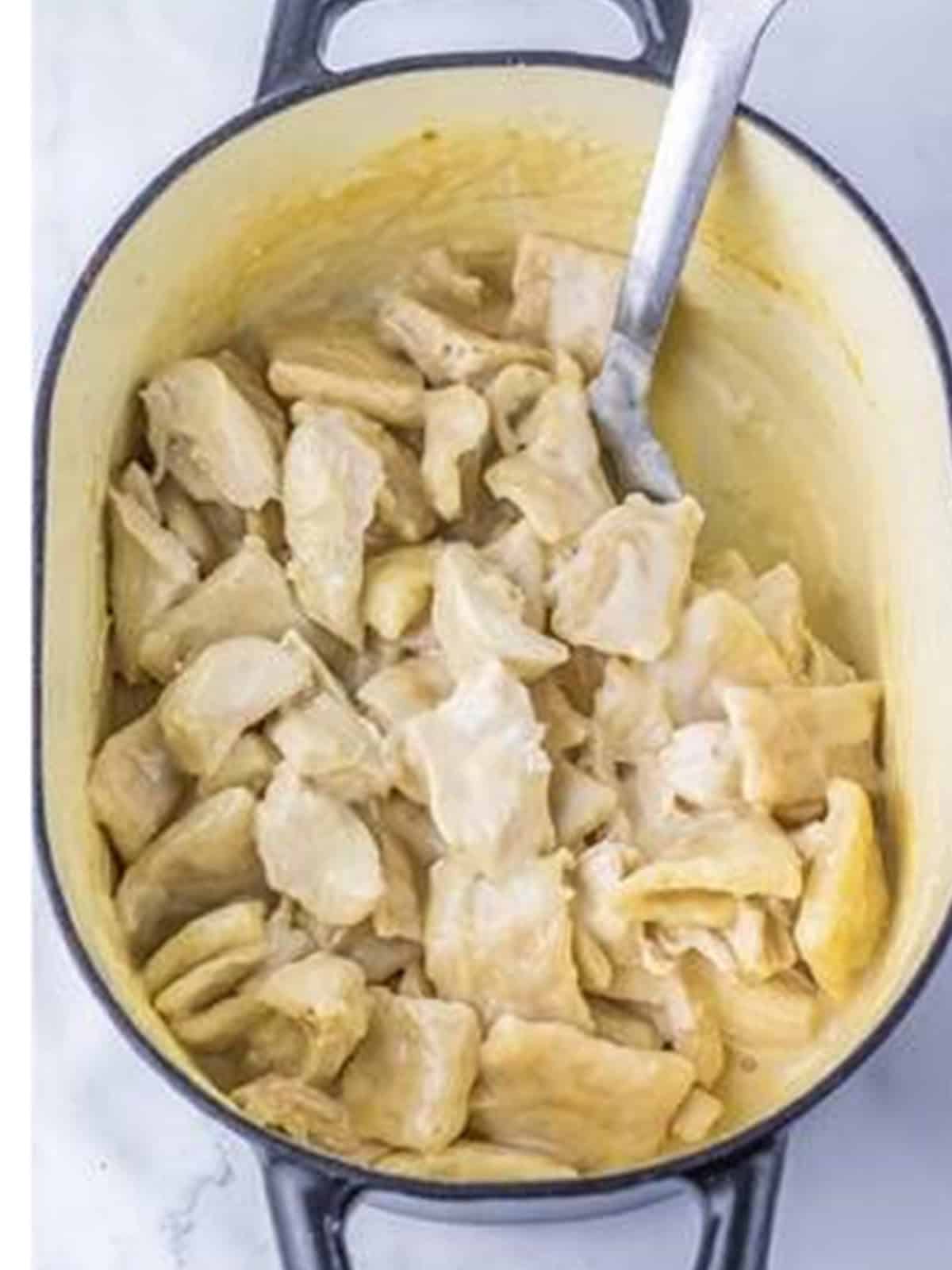 Finished creamy Cracker Barrel chicken and dumplings in a pot with a spoon.