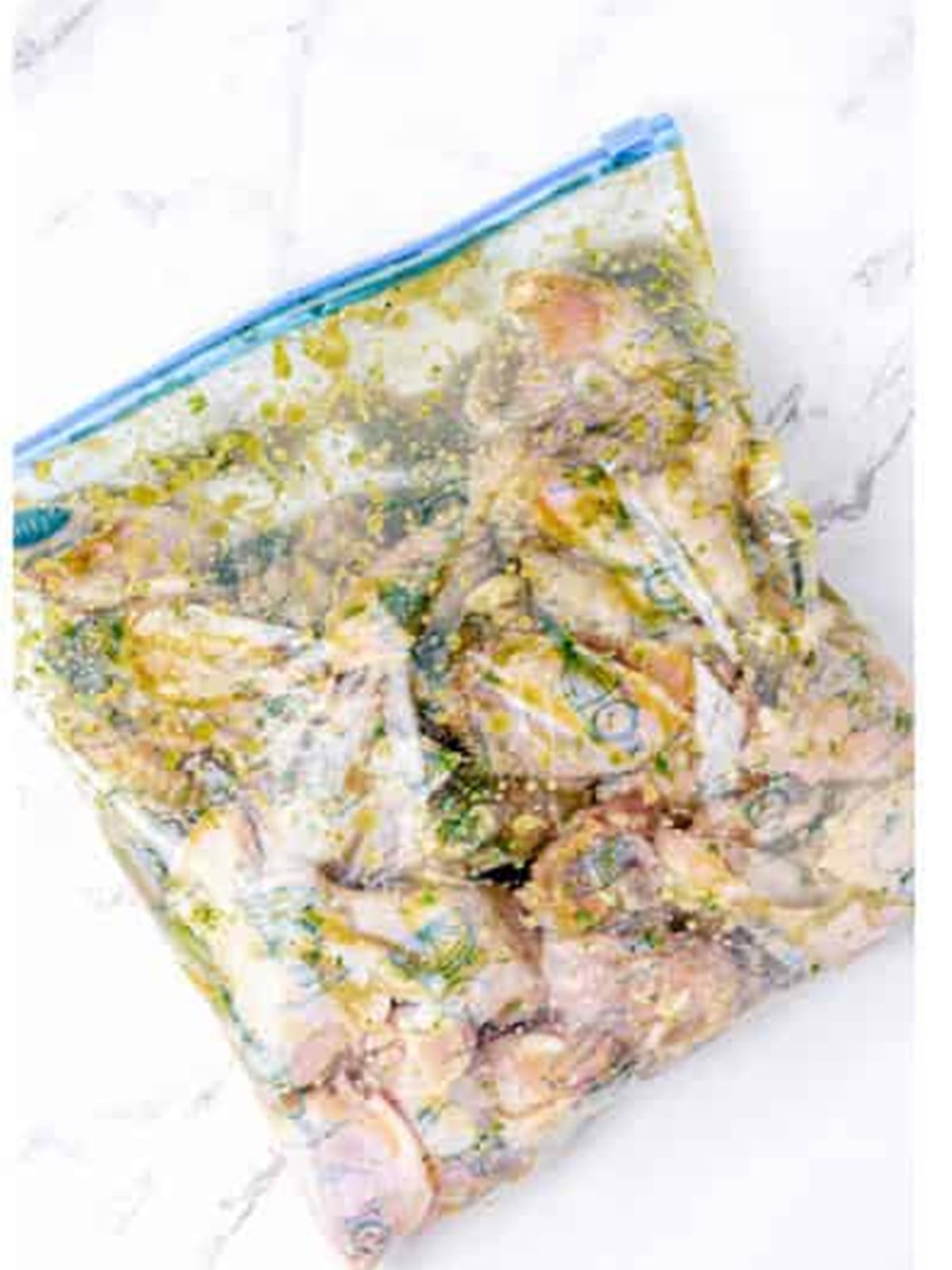 Chicken wings marinating in herb marinade in a sealed bag.