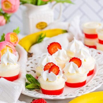Strawberry banana pudding shots topped with whipped cream and strawberry slices on a cake stand.