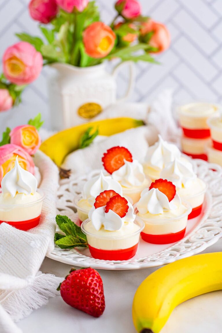 Strawberry banana pudding shots topped with whipped cream and strawberry slices on a cake stand.