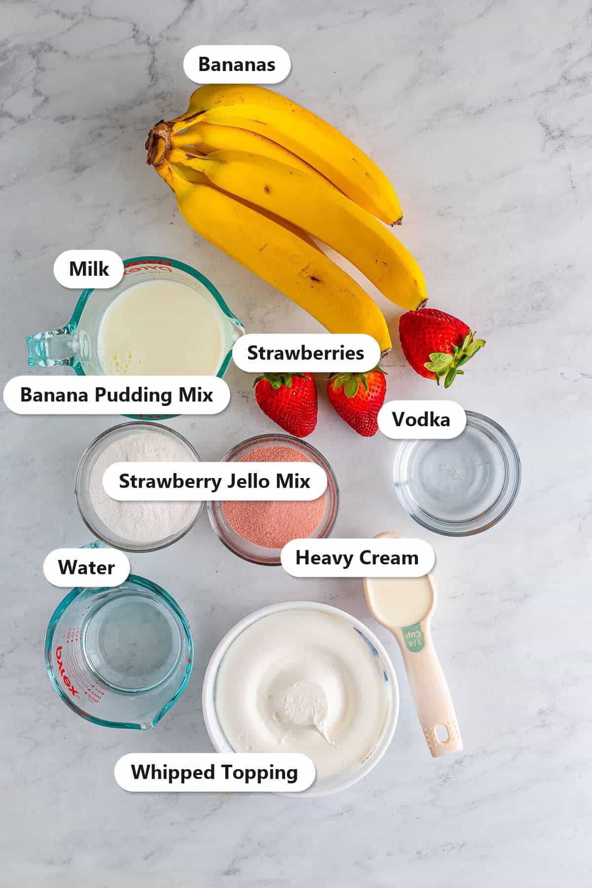 Labeled ingredients for strawberry banana pudding shots including strawberry jello mix, banana pudding mix, vodka, milk, heavy cream, whipped topping, bananas, and strawberries.
