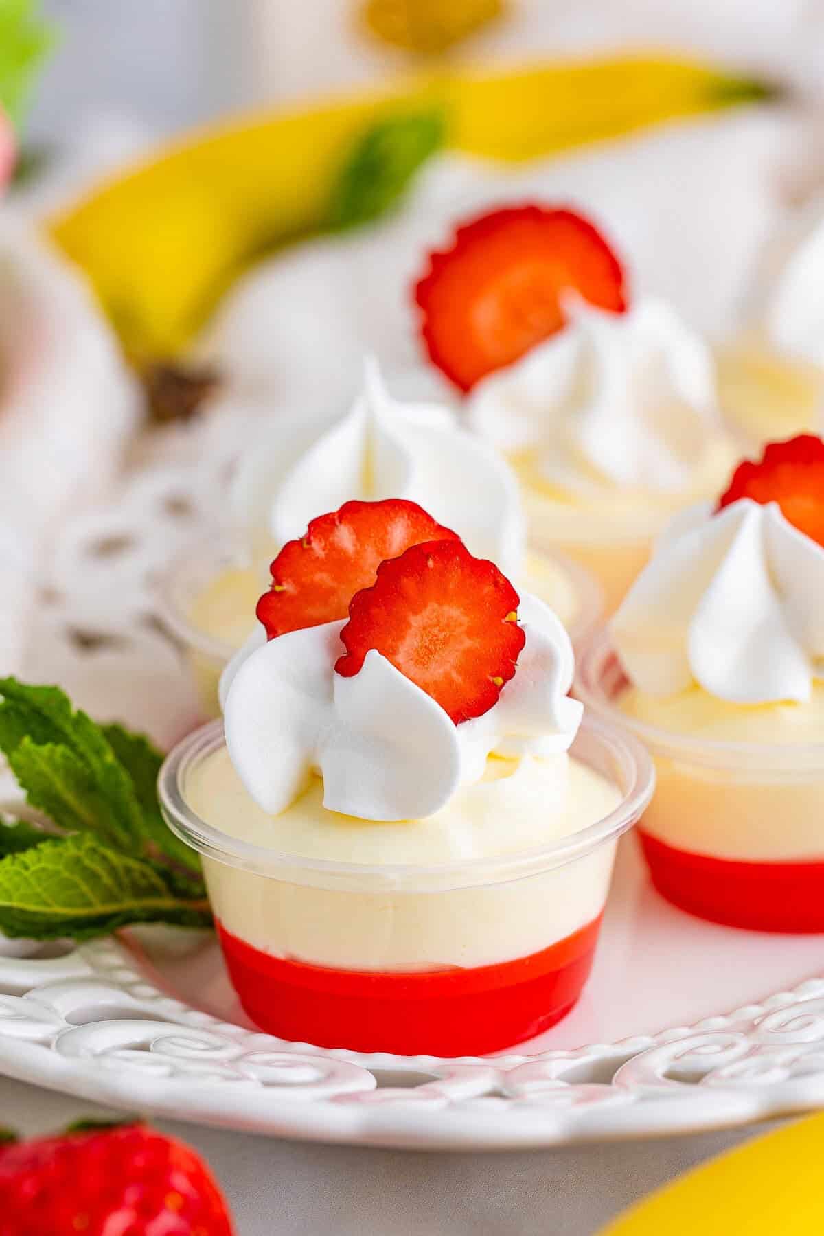 Layered strawberry banana pudding shots garnished with whipped topping and fresh fruit.