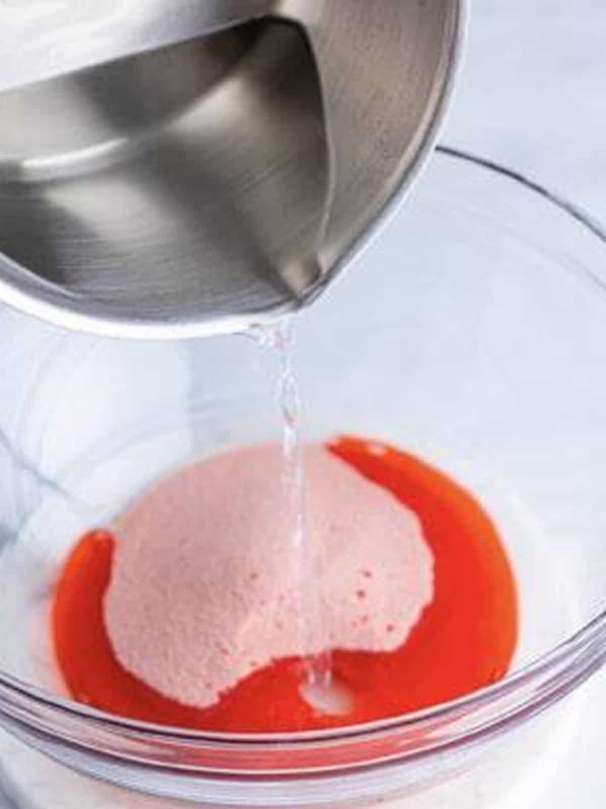 Boiling water poured into strawberry jello mix in a bowl.
