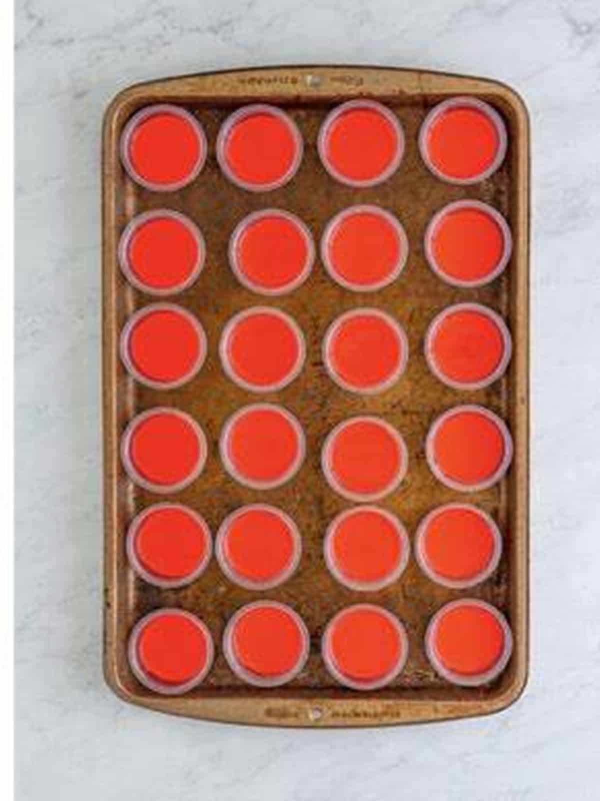 Strawberry jello mixture poured into plastic shot cups on a tray.