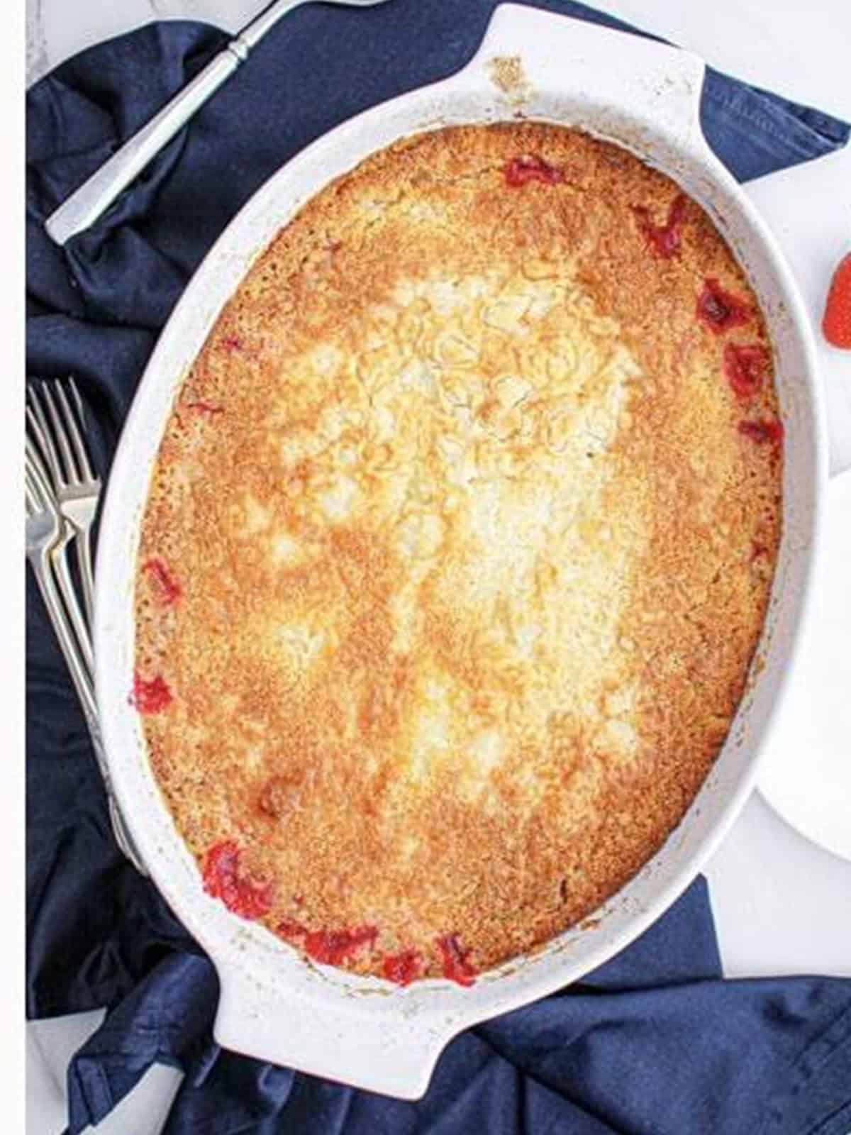 Golden baked strawberry cheesecake dump cake in a white baking dish.