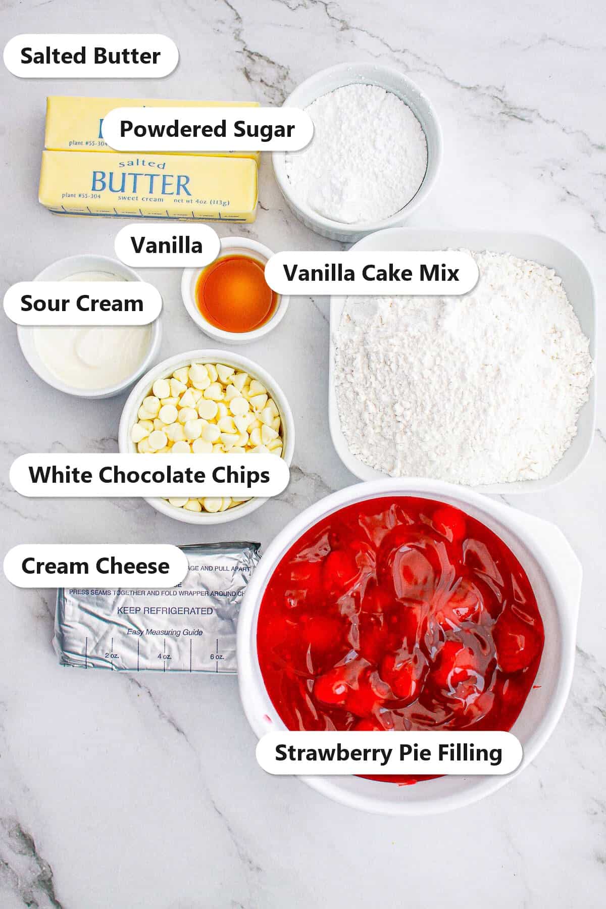 Labeled ingredients for strawberry cheesecake dump cake including cream cheese, strawberry pie filling, vanilla cake mix, white chocolate chips, butter, powdered sugar, sour cream, and vanilla.