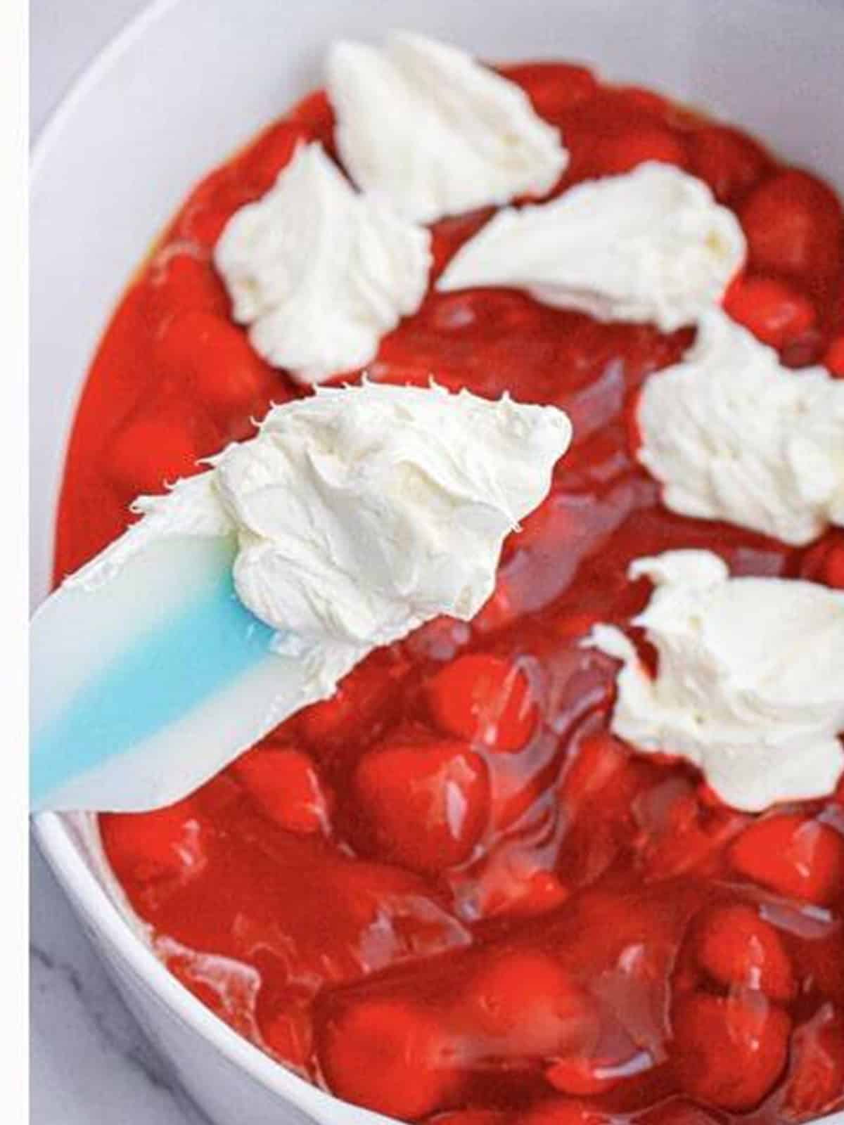 Spoonfuls of cream cheese mixture dropped over strawberry pie filling in a baking dish.