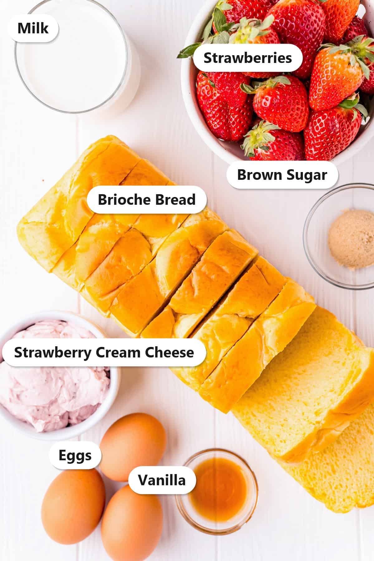 Labeled ingredients for Strawberry Cheesecake Stuffed French Toast including brioche bread, strawberry cream cheese, eggs, milk, brown sugar, vanilla, and strawberries.
