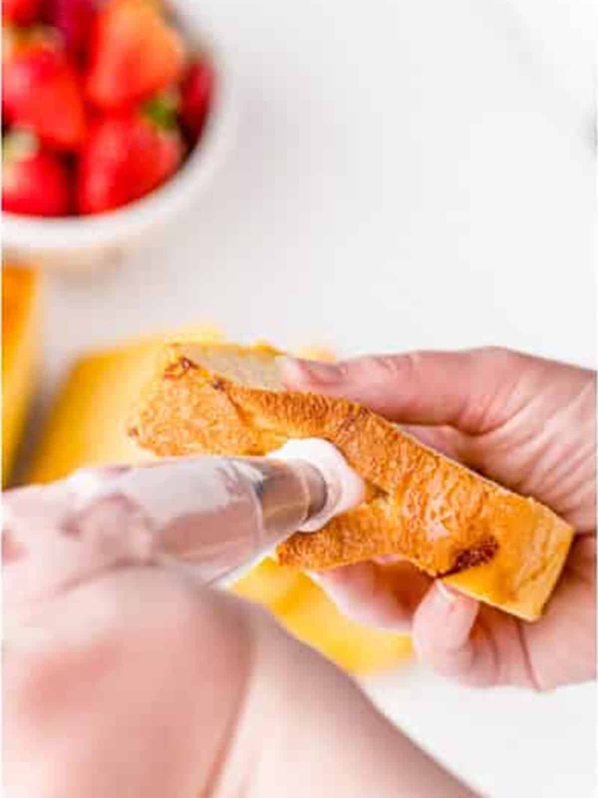Piping strawberry cream cheese into a slit in a brioche slice.