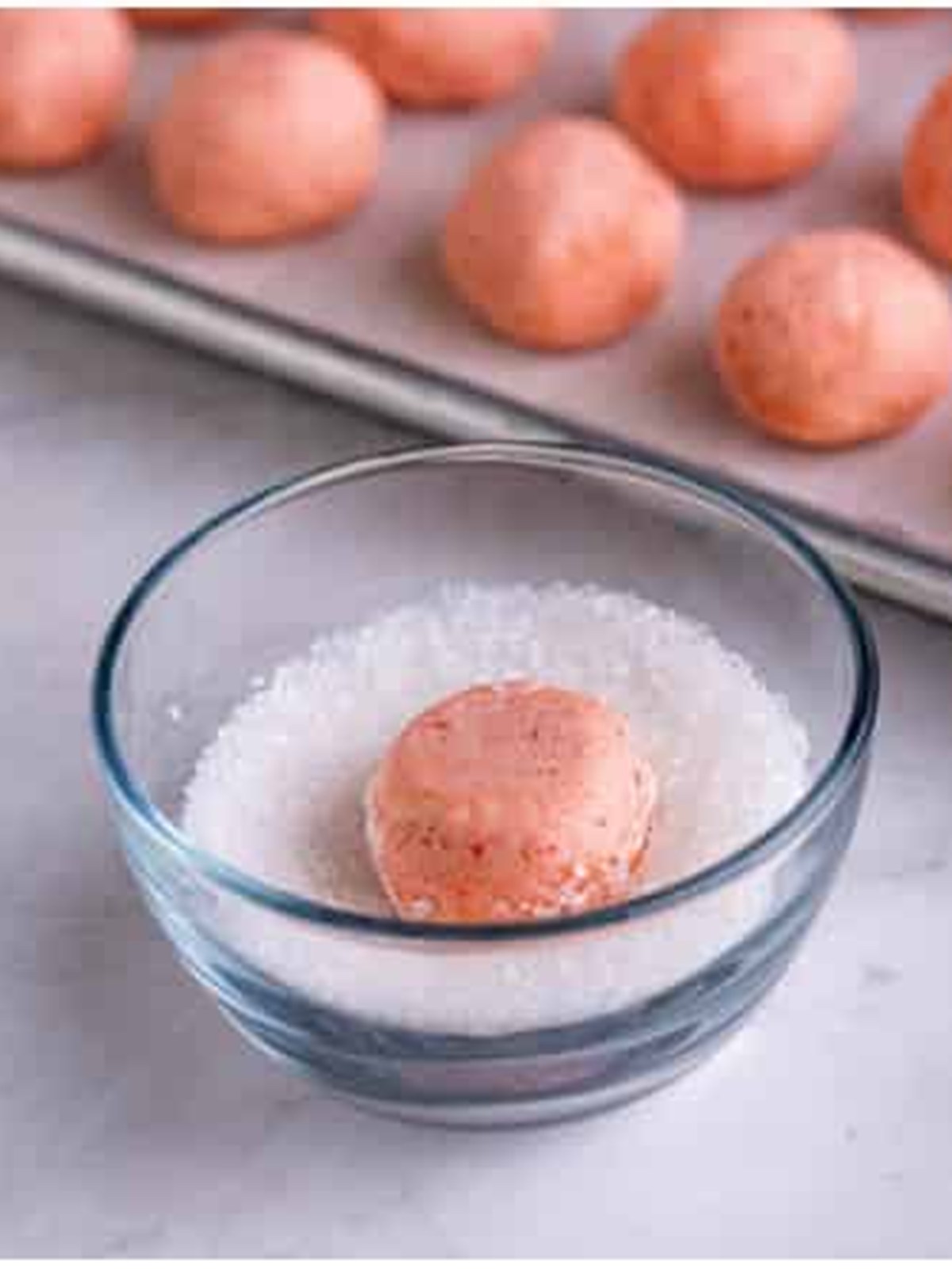 Dipping a Strawberry Cookies dough ball into decorators sugar.
