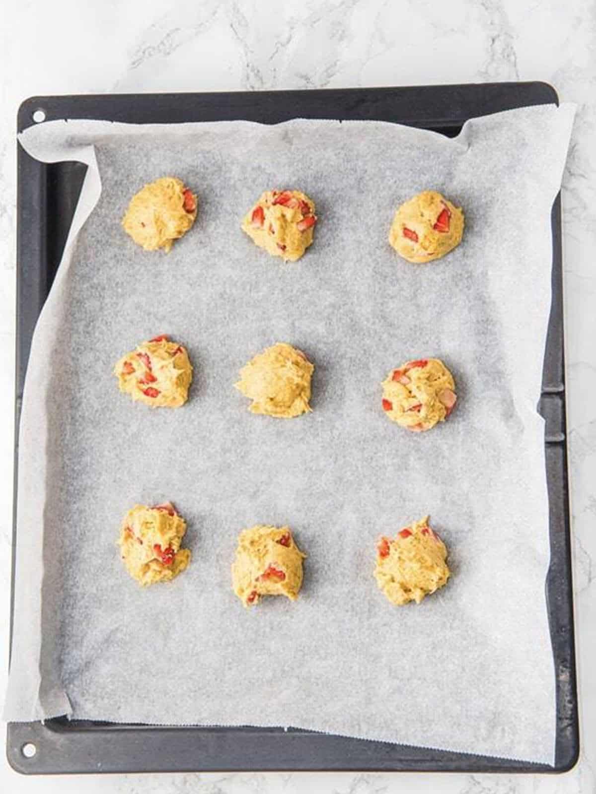 Scoops of strawberry cookie dough on a parchment lined baking sheet.