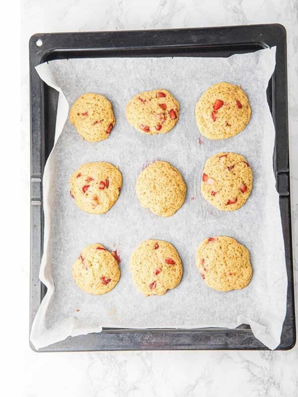 Baked fresh strawberry cookies on a parchment lined baking sheet.