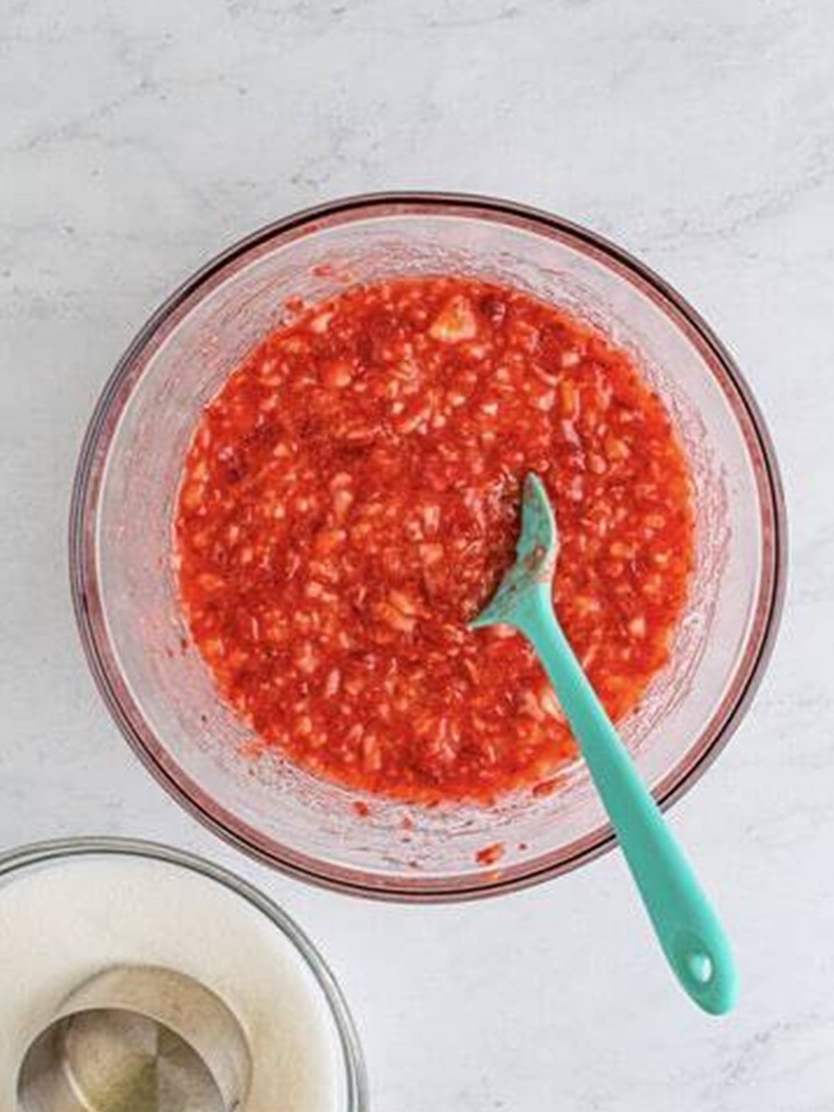 Stirring sugar into the crushed strawberries until dissolved.