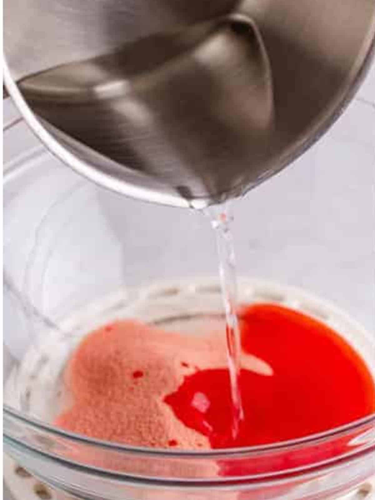 Boiling water poured over strawberry jello powder to dissolve it.