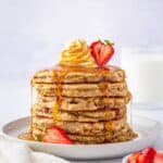 A stack of strawberry oatmeal pancakes drizzled with maple syrup and topped with fresh strawberries.