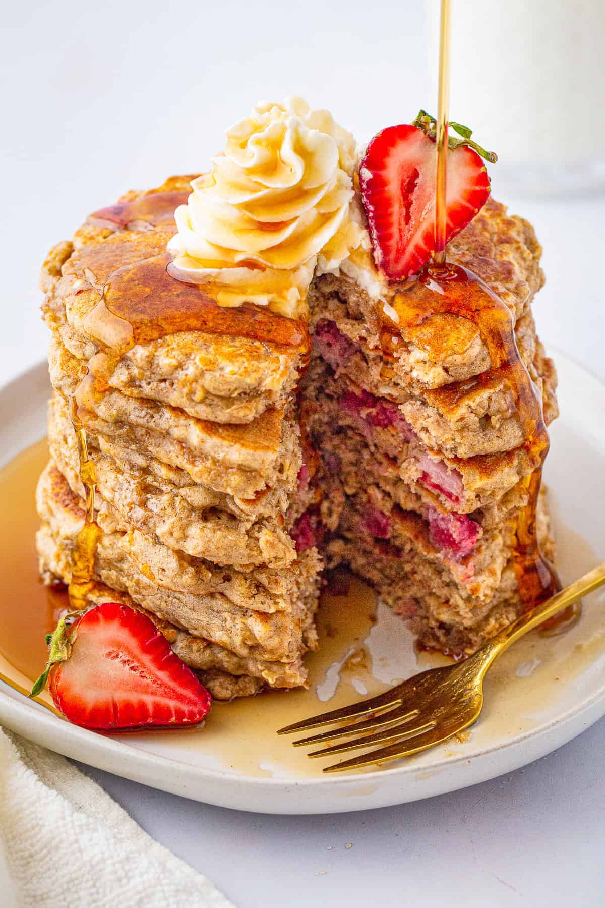 A stack of strawberry oatmeal pancakes with a bite taken out showing the fluffy interior with strawberries.