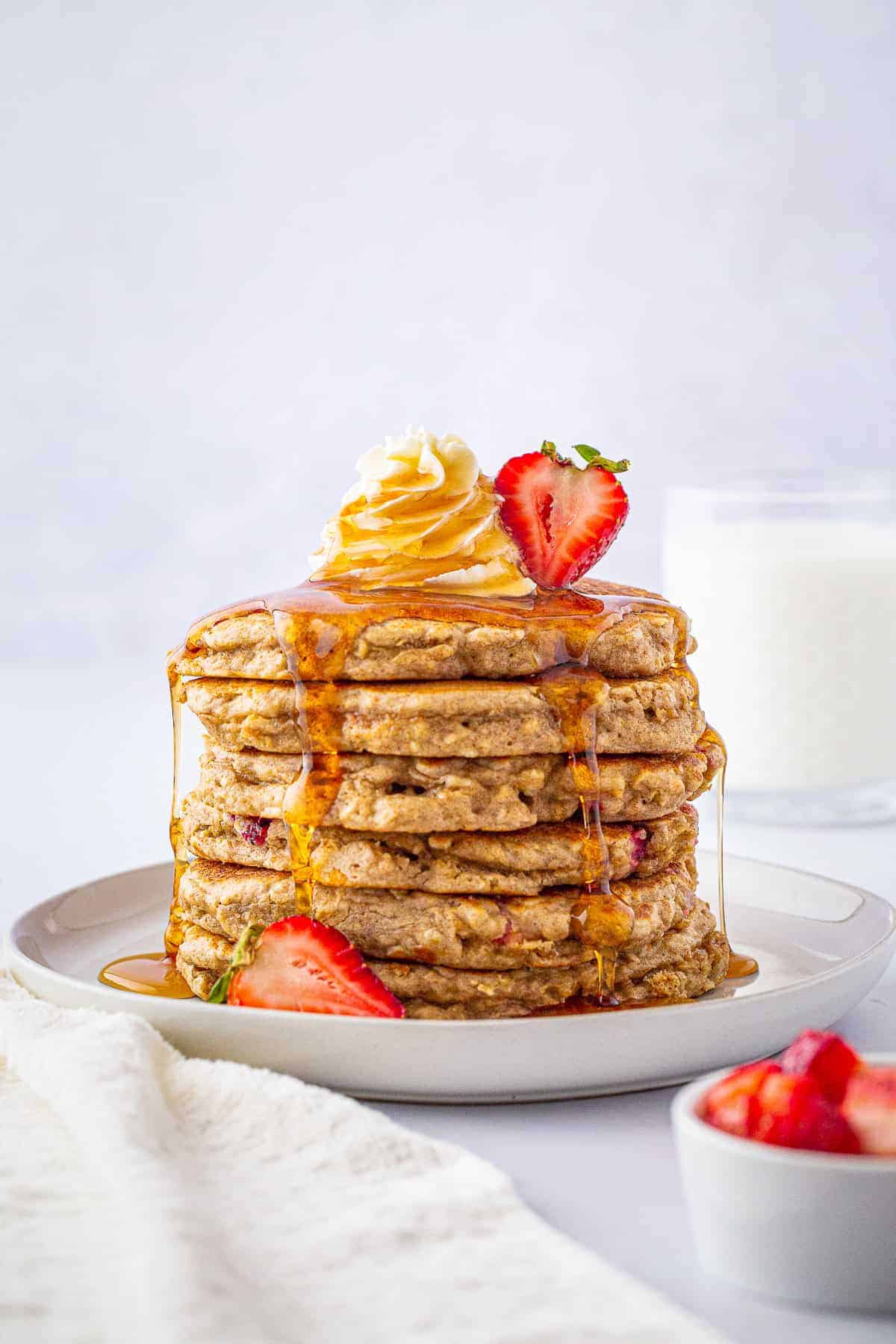 A stack of strawberry oatmeal pancakes drizzled with maple syrup and topped with fresh strawberries.