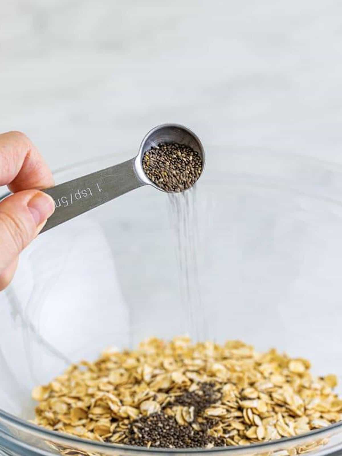 Old-fashioned oats and chia seeds added to a glass bowl for strawberry overnight oats.