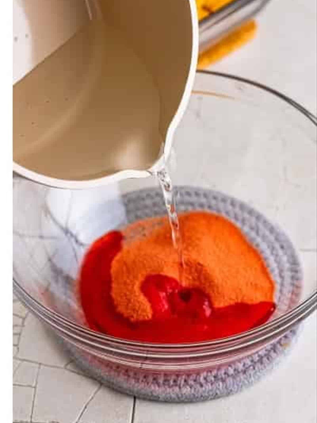 Pouring boiling water over strawberry jello for poke cake.