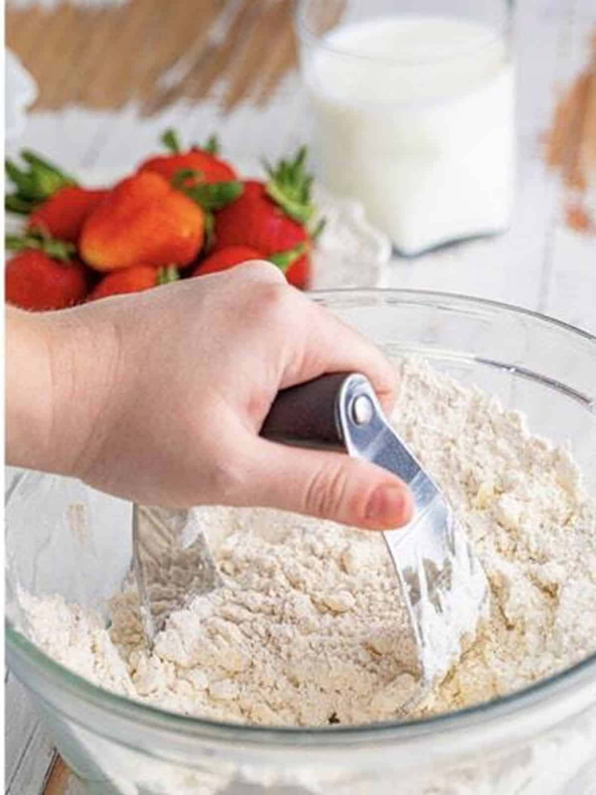 Cold butter being cut into the flour mixture with a pastry cutter.