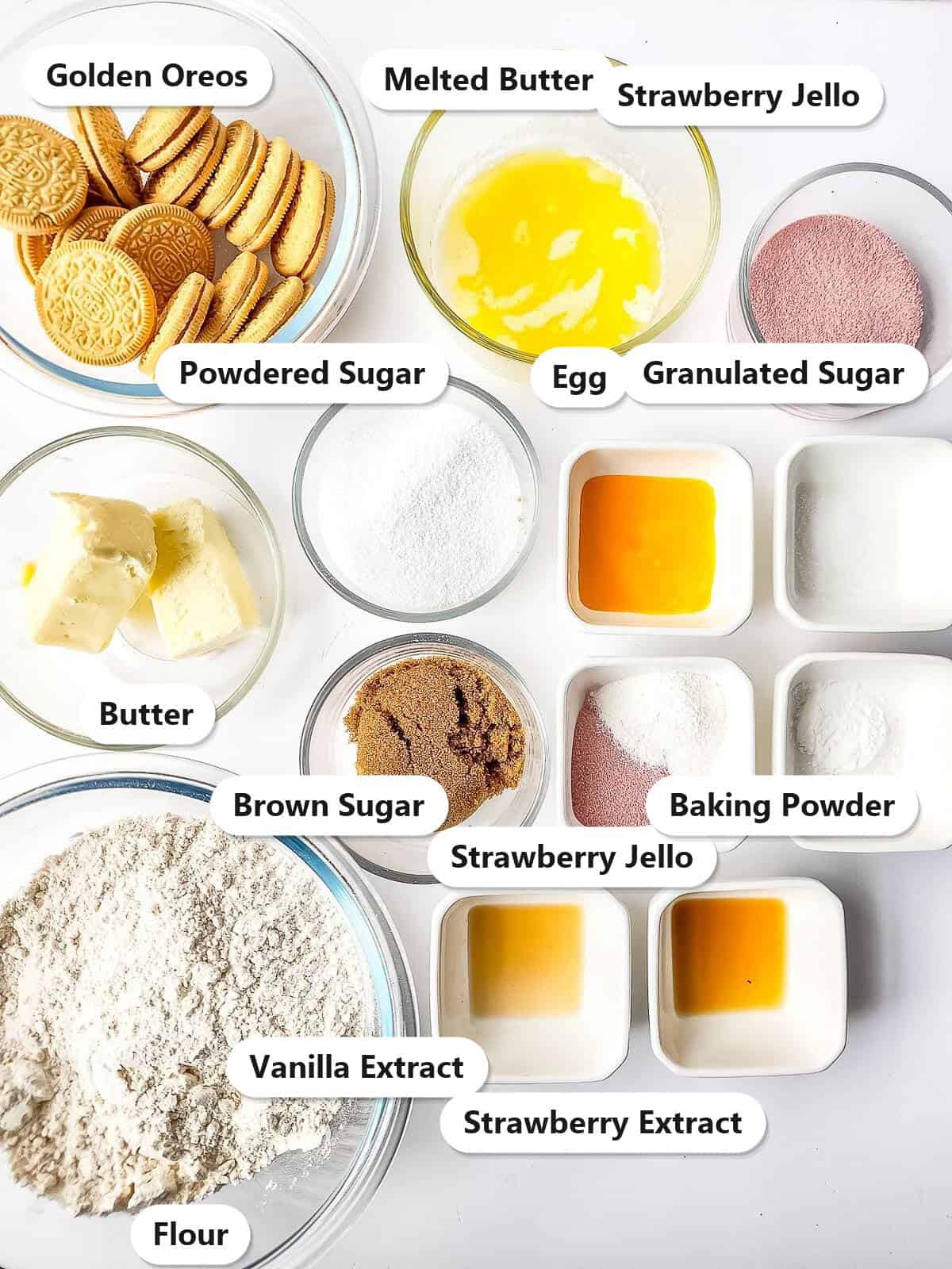 Labeled ingredients to make strawberry shortcake cookies including butter, sugars, egg, flour, strawberry jello, golden Oreos, and cream cheese frosting fixings.