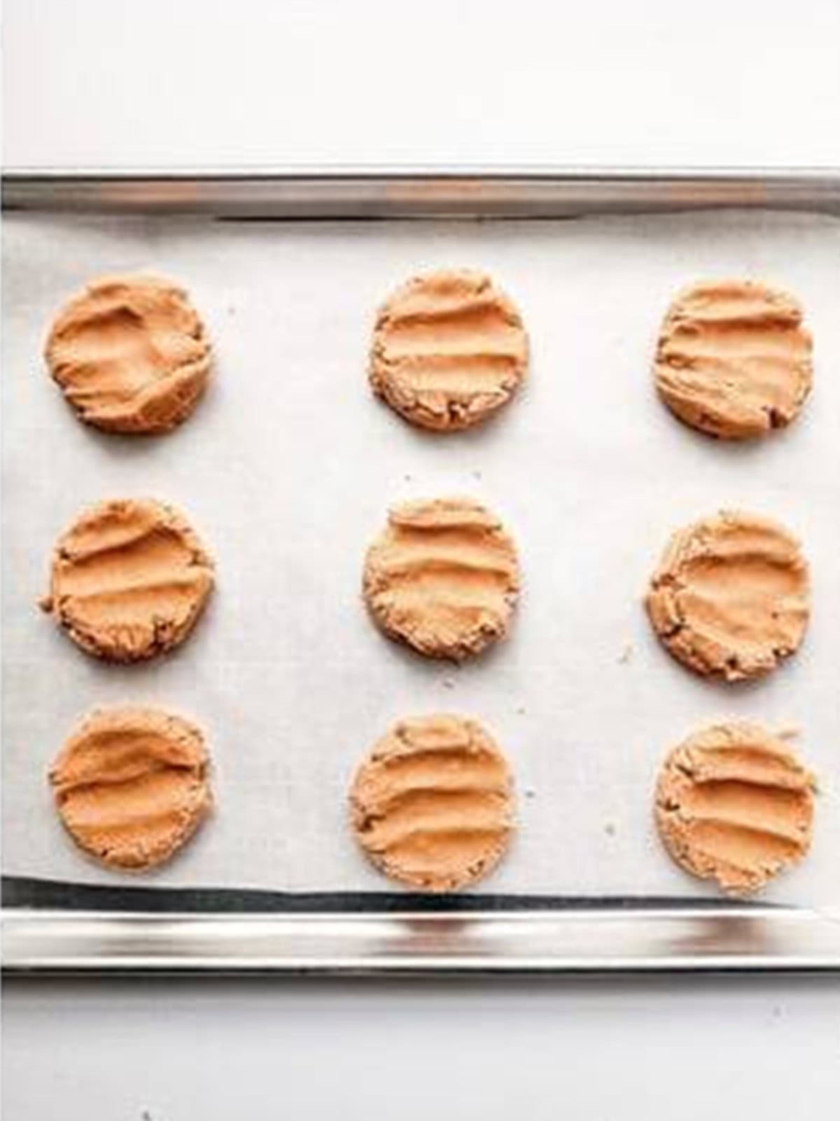 Portioned and flattened strawberry shortcake cookie dough on a parchment lined baking sheet.