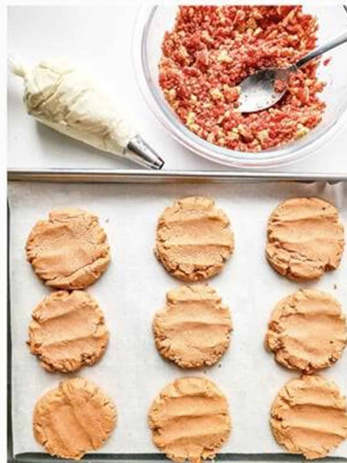 Baked strawberry shortcake cookies cooling next to frosting and strawberry crunch.