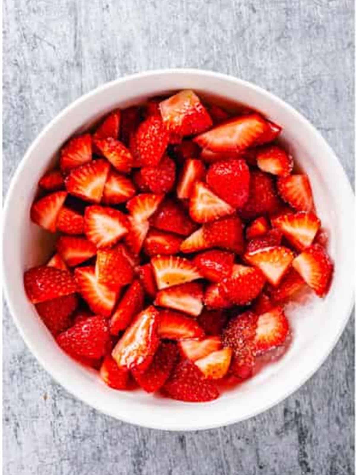 Sliced strawberries tossed with sugar in a bowl to macerate for strawberry shortcake.