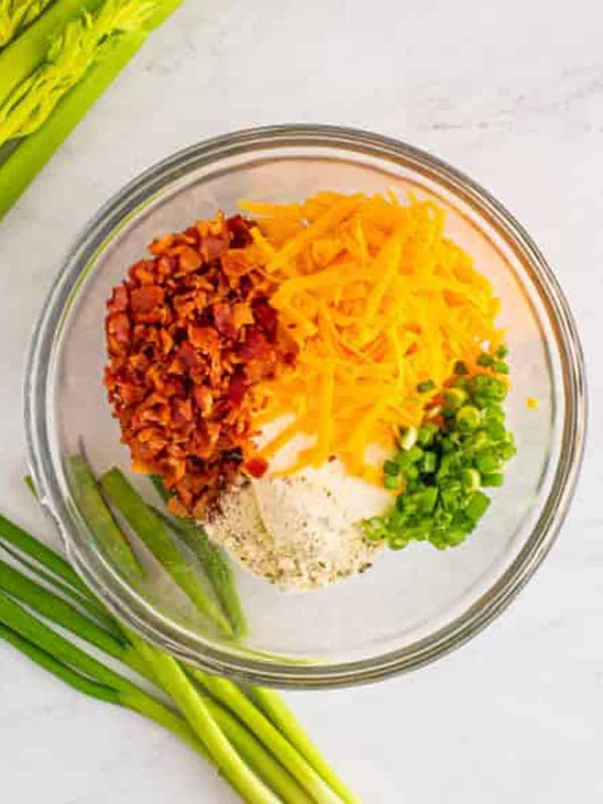 Cream cheese, cheddar, ranch seasoning, bacon, and scallions combined in a bowl for the celery filling.