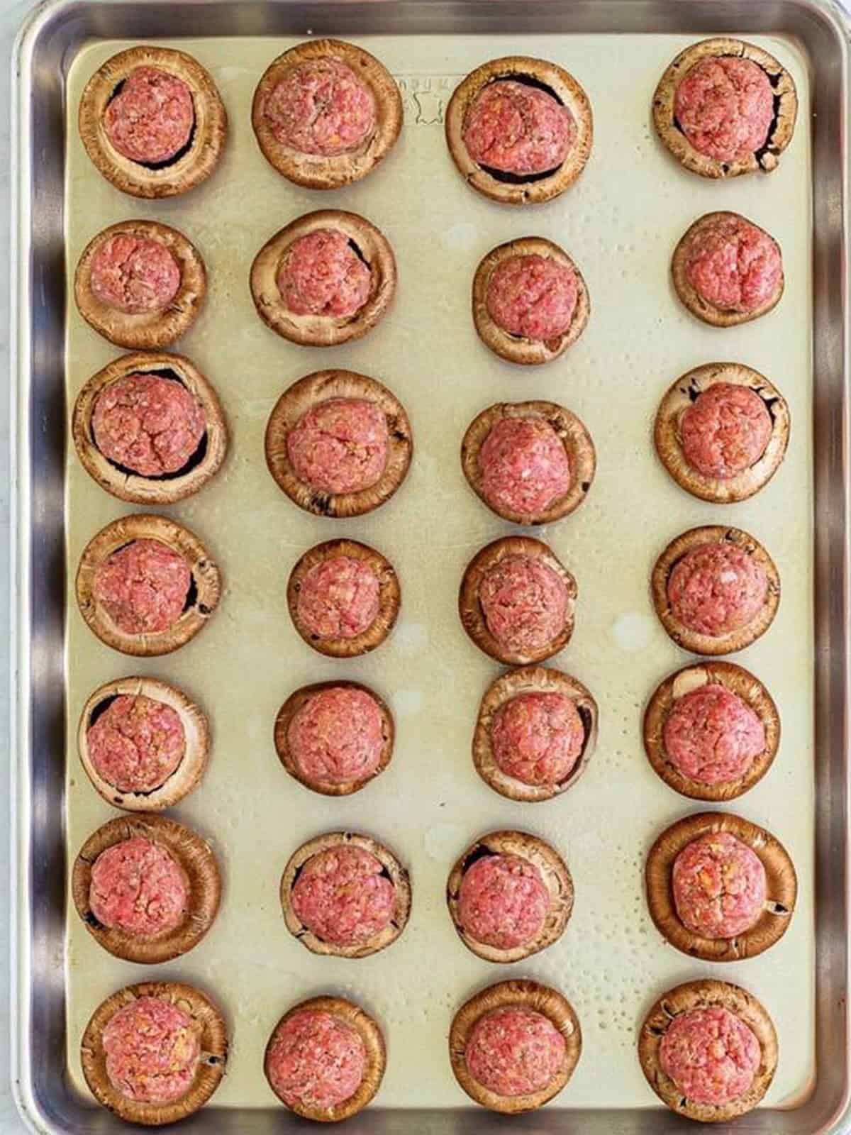 Mushroom caps topped with raw meatballs on a sheet pan.
