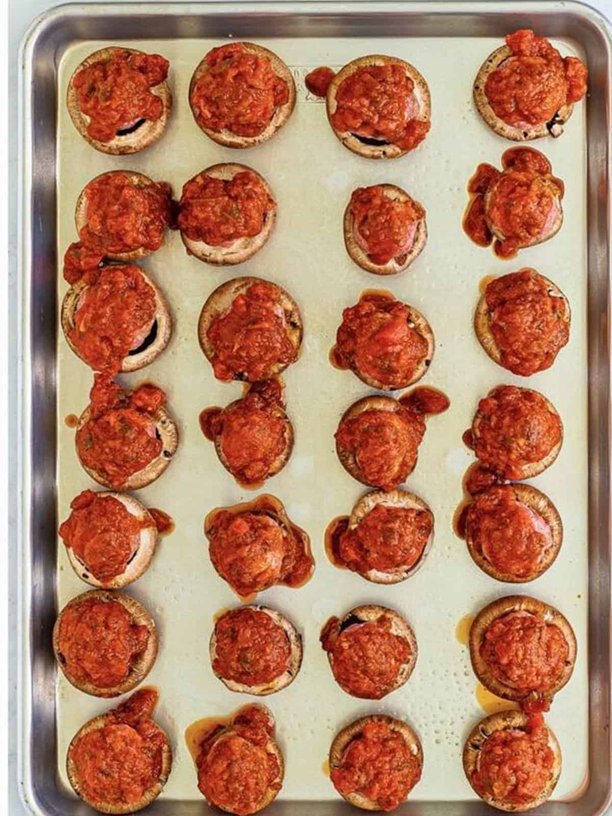 Meatball stuffed mushrooms topped with marinara sauce before baking.