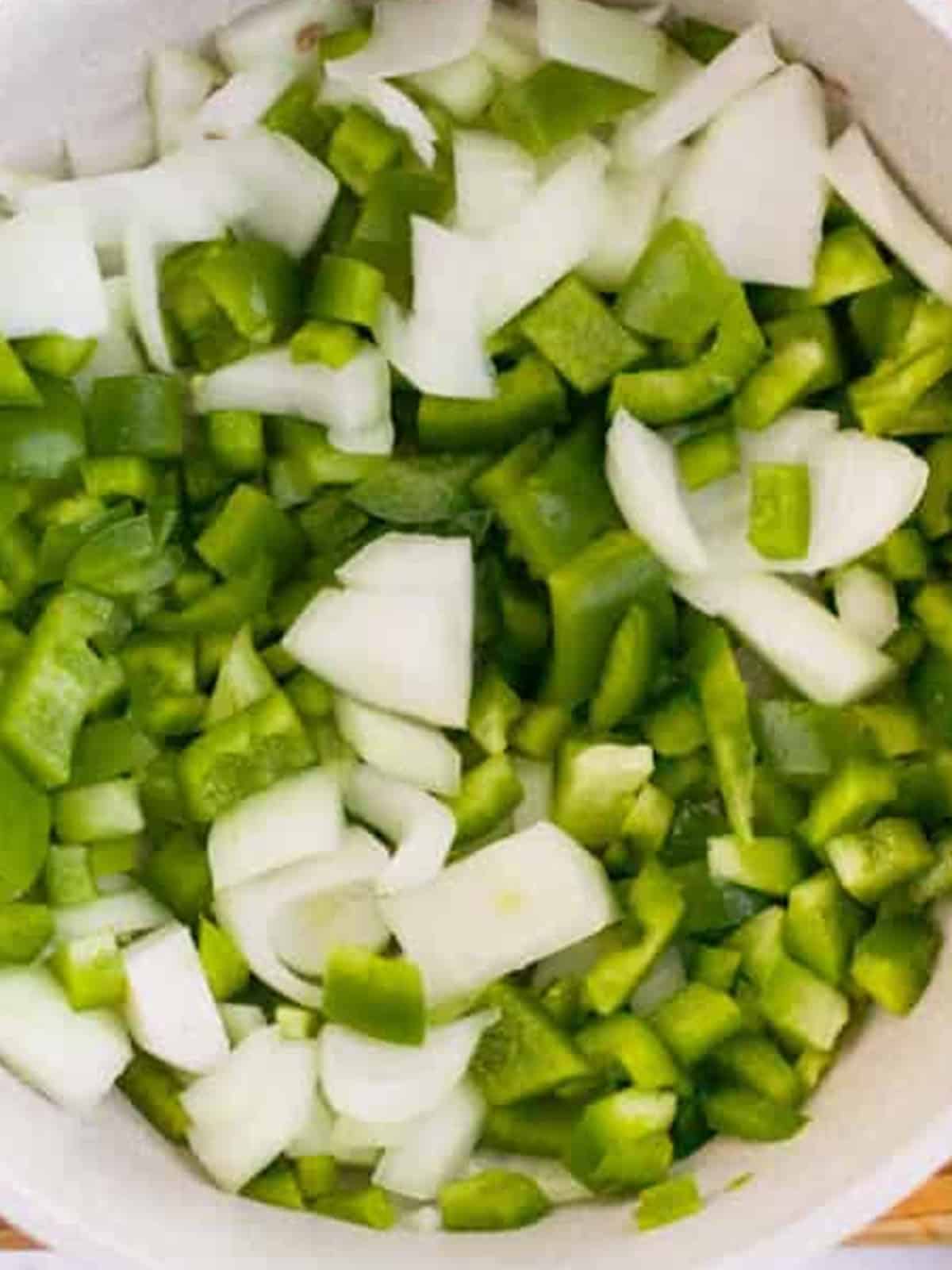 Chopped green bell peppers and onion cooking in a pot for stuffed pepper soup.