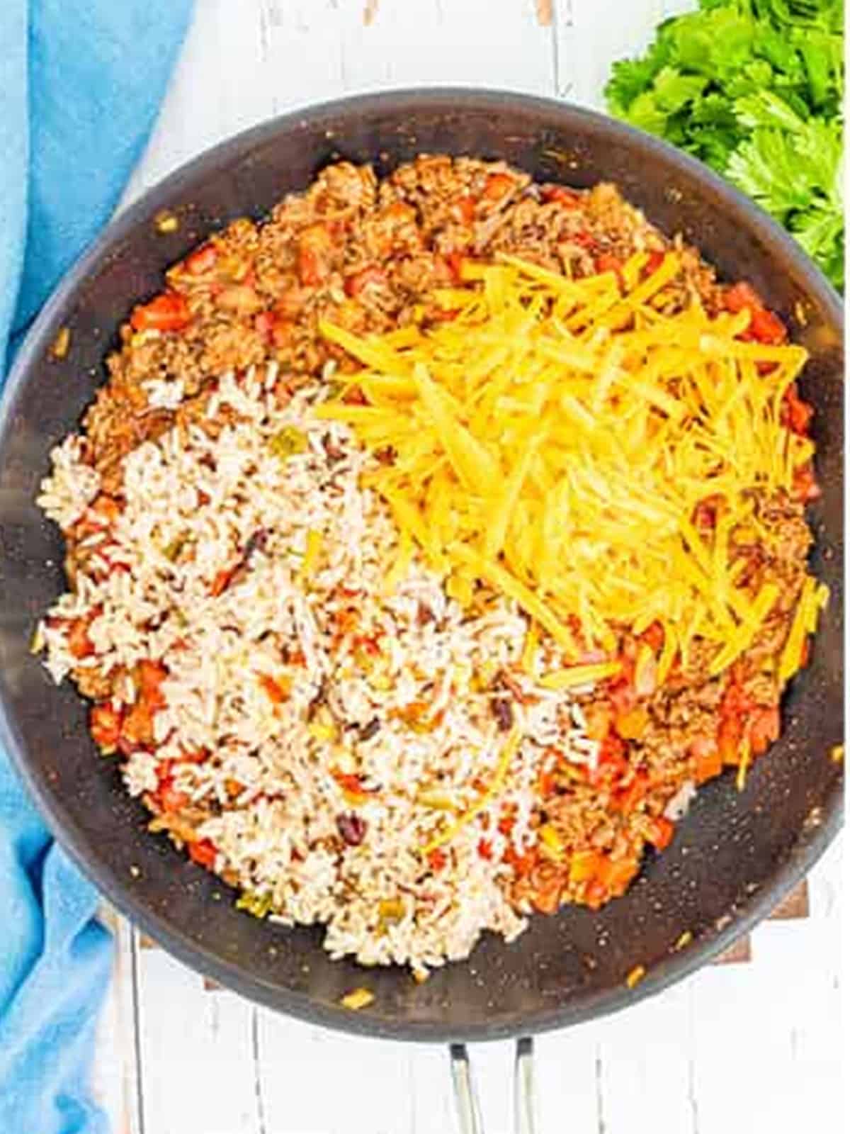 Adding rice, beans, diced tomatoes, and cheese to the ground beef to make stuffed pepper filling.