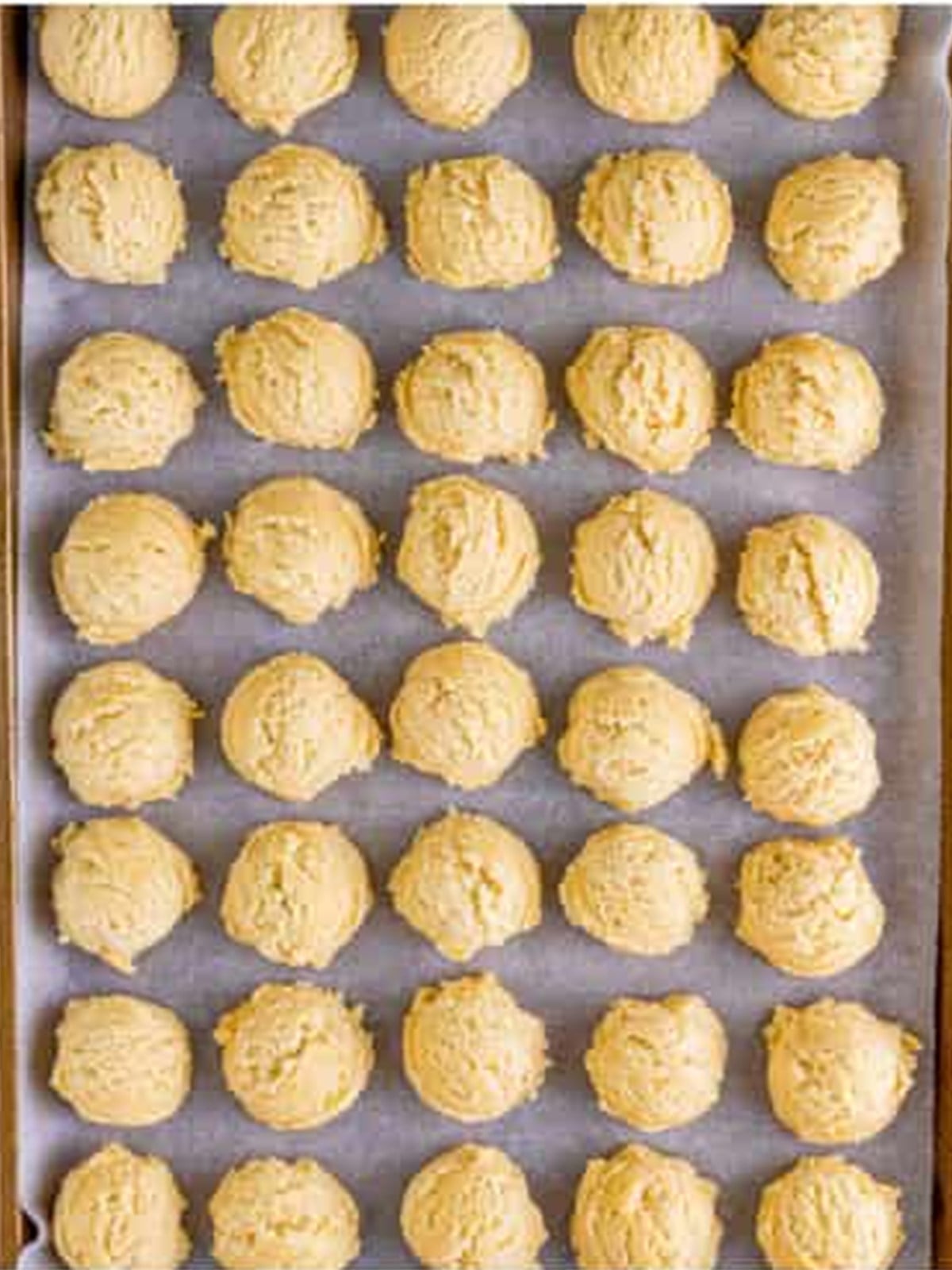 Scooped sugar cookie dough balls on a parchment-lined baking tray