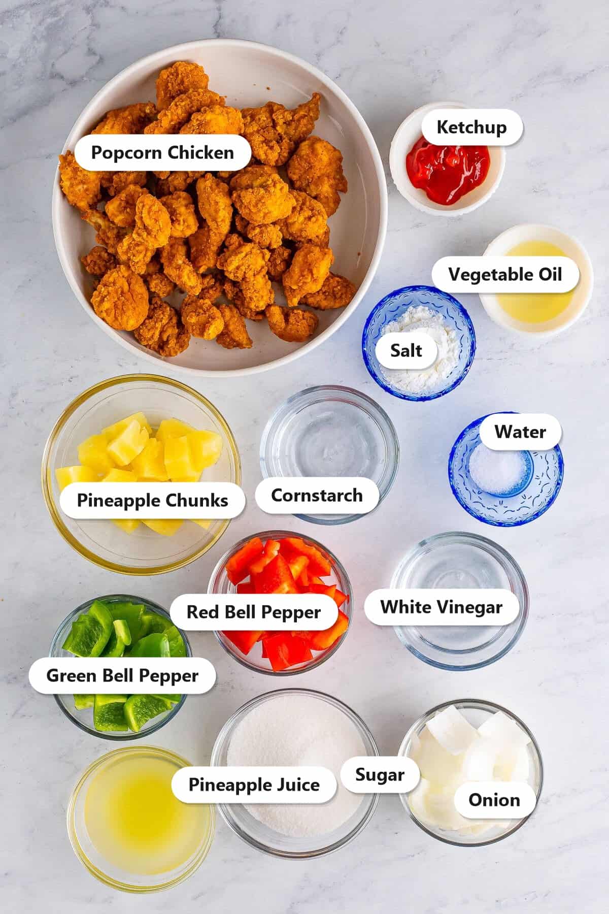 Labeled ingredients to make sweet and sour chicken including popcorn chicken, bell peppers, onion, pineapple, and sweet and sour sauce components.