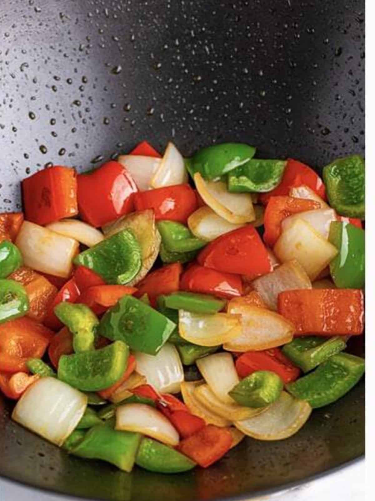 Diced green and red bell peppers and onion stir-frying in a wok for sweet and sour chicken.
