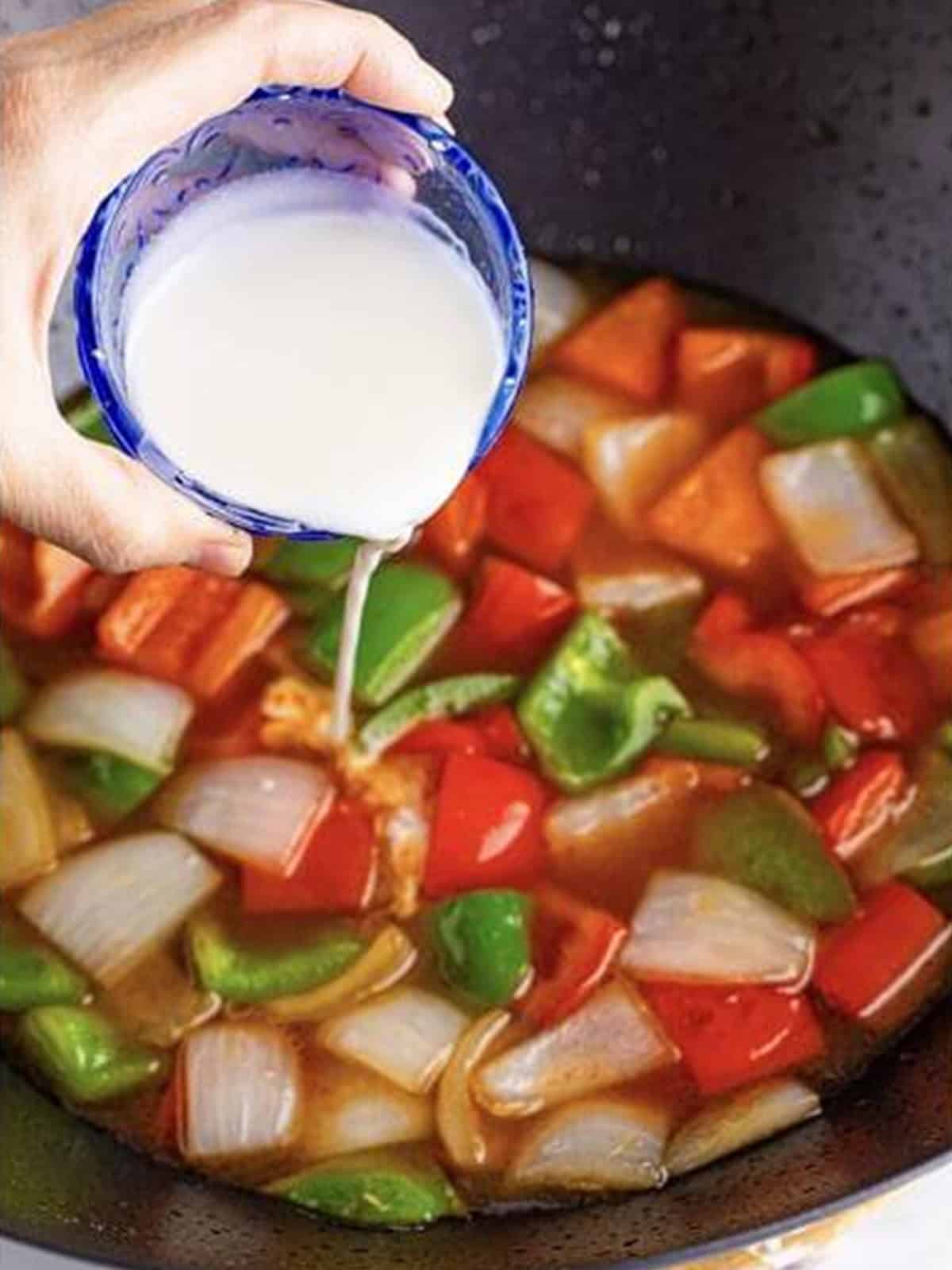 Cornstarch slurry being poured into the simmering sweet and sour sauce.